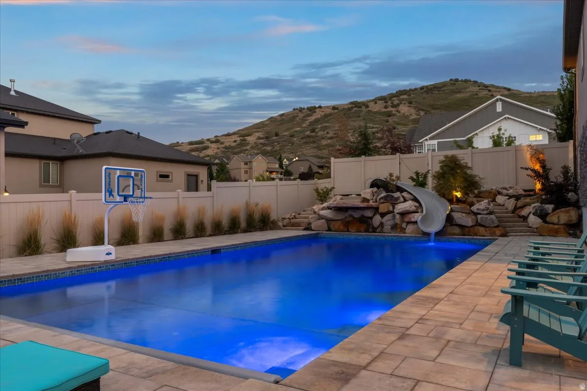 View of pool featuring a fenced backyard, patio surround, a mountain view, and a water slide