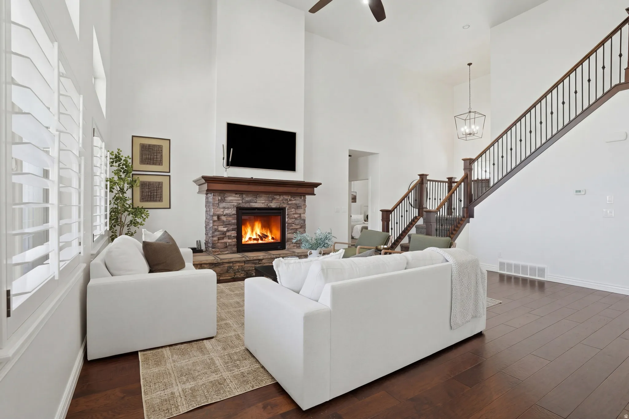 Living room featuring dark wood finished floors, a stone fireplace, a high ceiling, and a ceiling fan