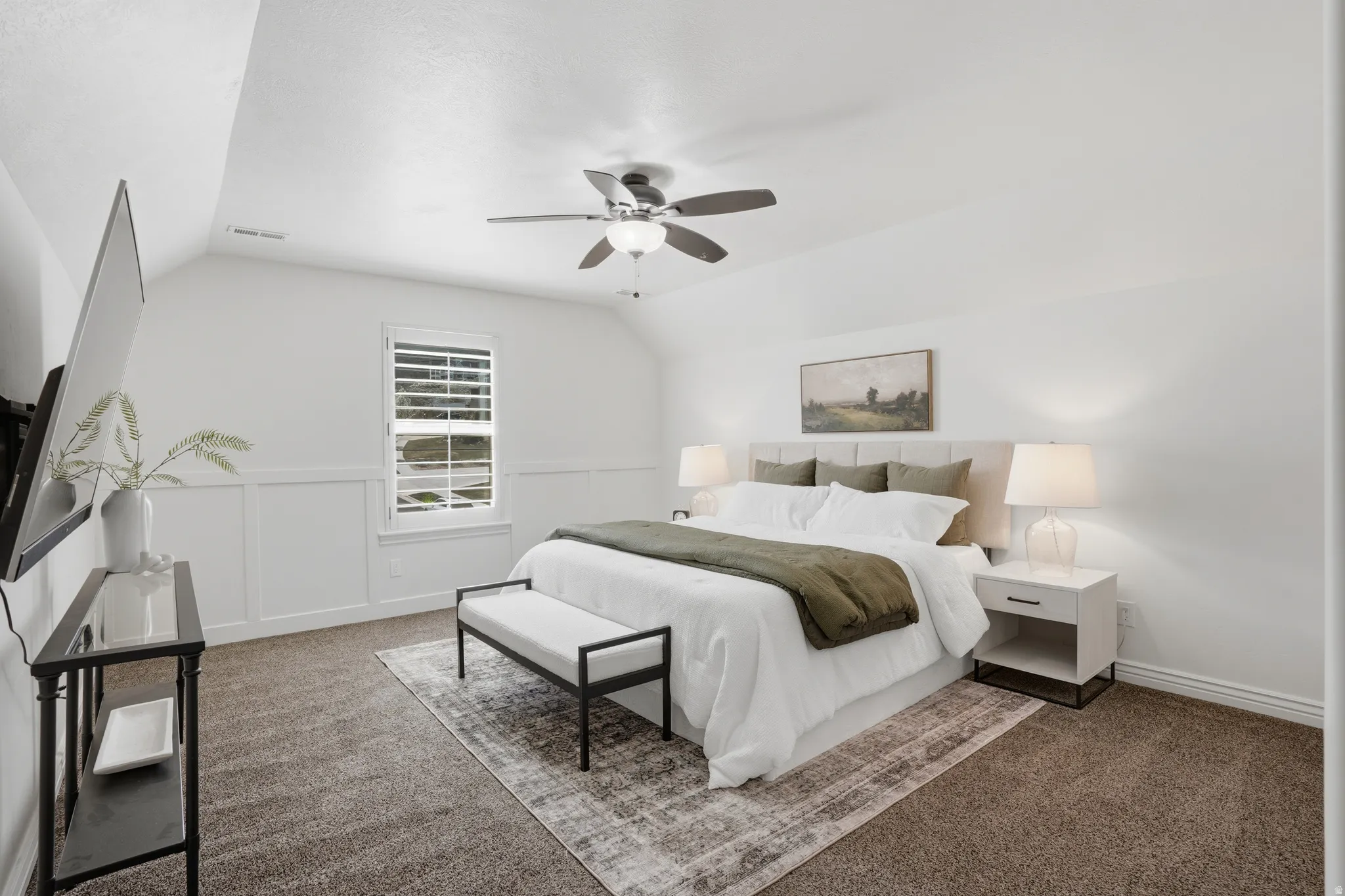 Bedroom with dark colored carpet, a ceiling fan, vaulted ceiling, a decorative wall, and wainscoting