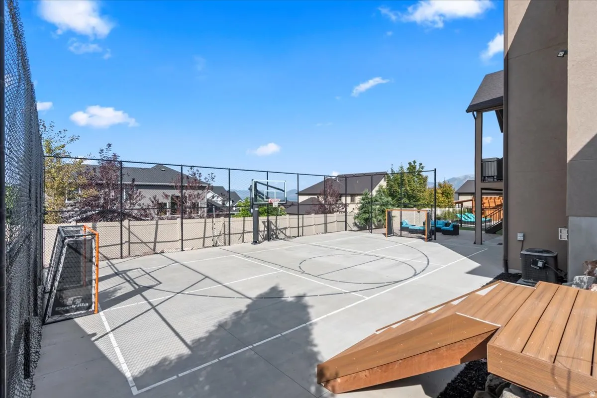 View of sport court featuring basketball hoop, a balcony, a residential view, and a patio