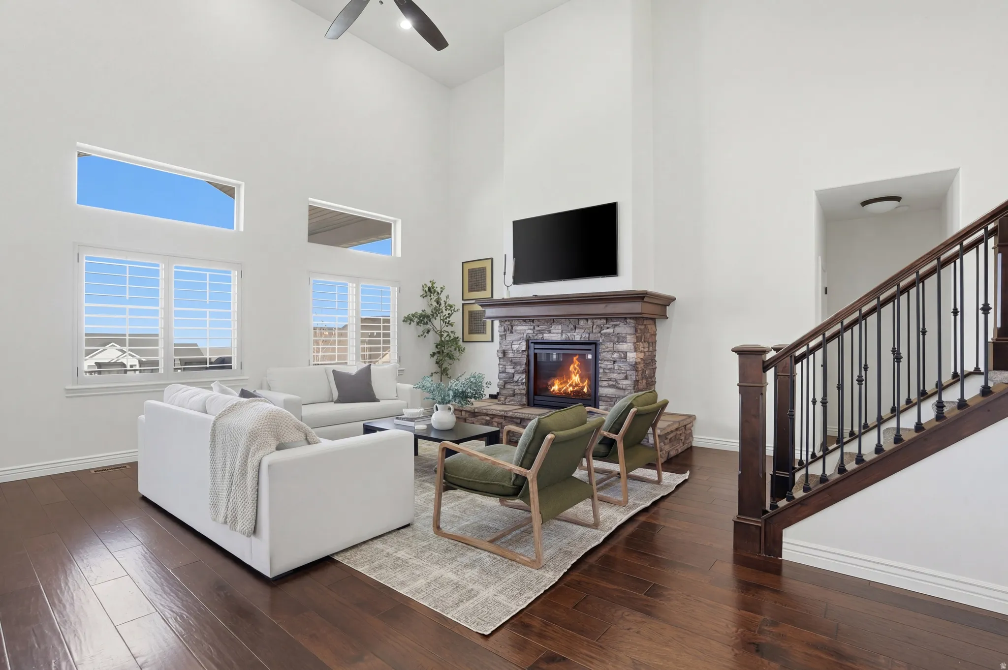 Living room featuring a high ceiling, dark wood finished floors, a fireplace, and ceiling fan