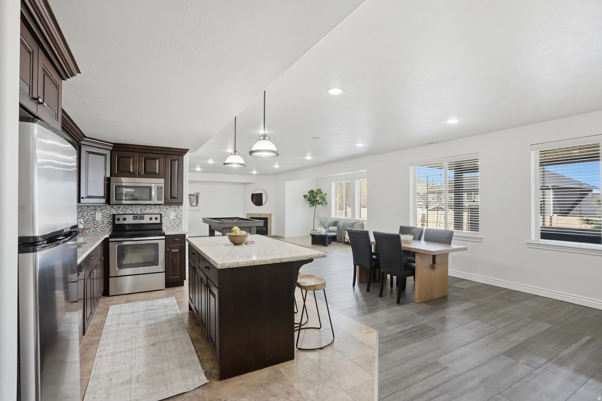 Kitchen with stainless steel appliances, a center island, tasteful backsplash, dark wood finish cabinetry, and light stone countertops