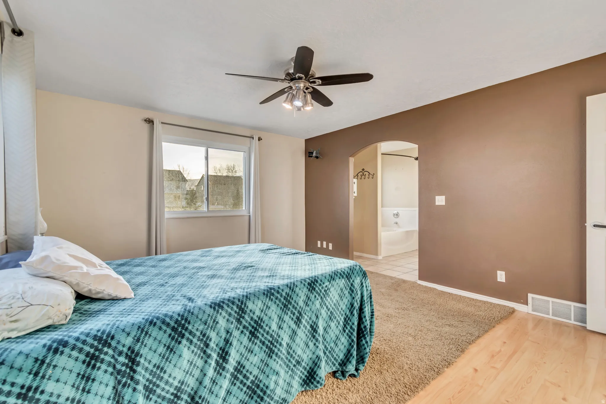 Bedroom with ceiling fan, light wood-style floors, arched walkways, connected bathroom, and light colored carpet