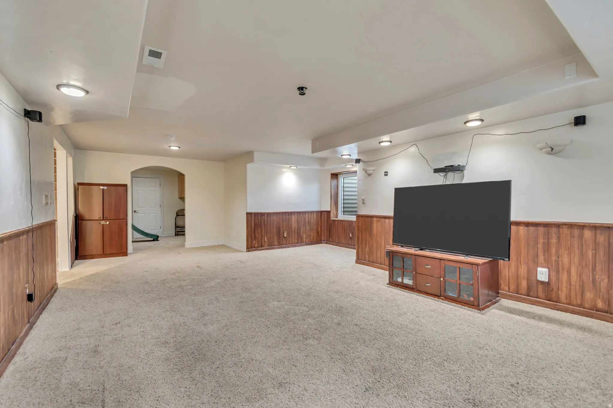 Unfurnished living room featuring wooden walls, arched walkways, a wainscoted wall, and light carpet