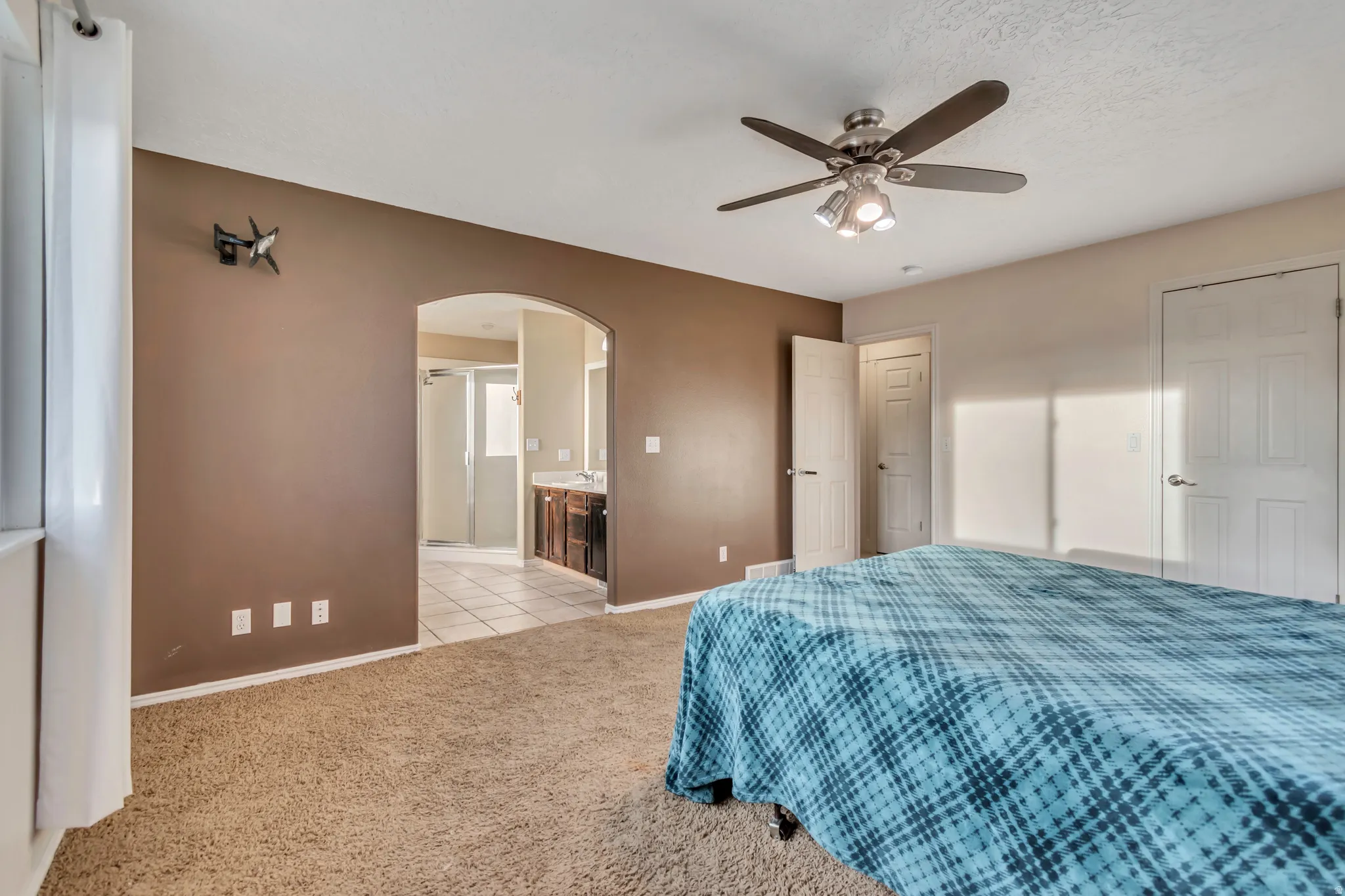 Bedroom with arched walkways, a ceiling fan, light carpet, and connected bathroom