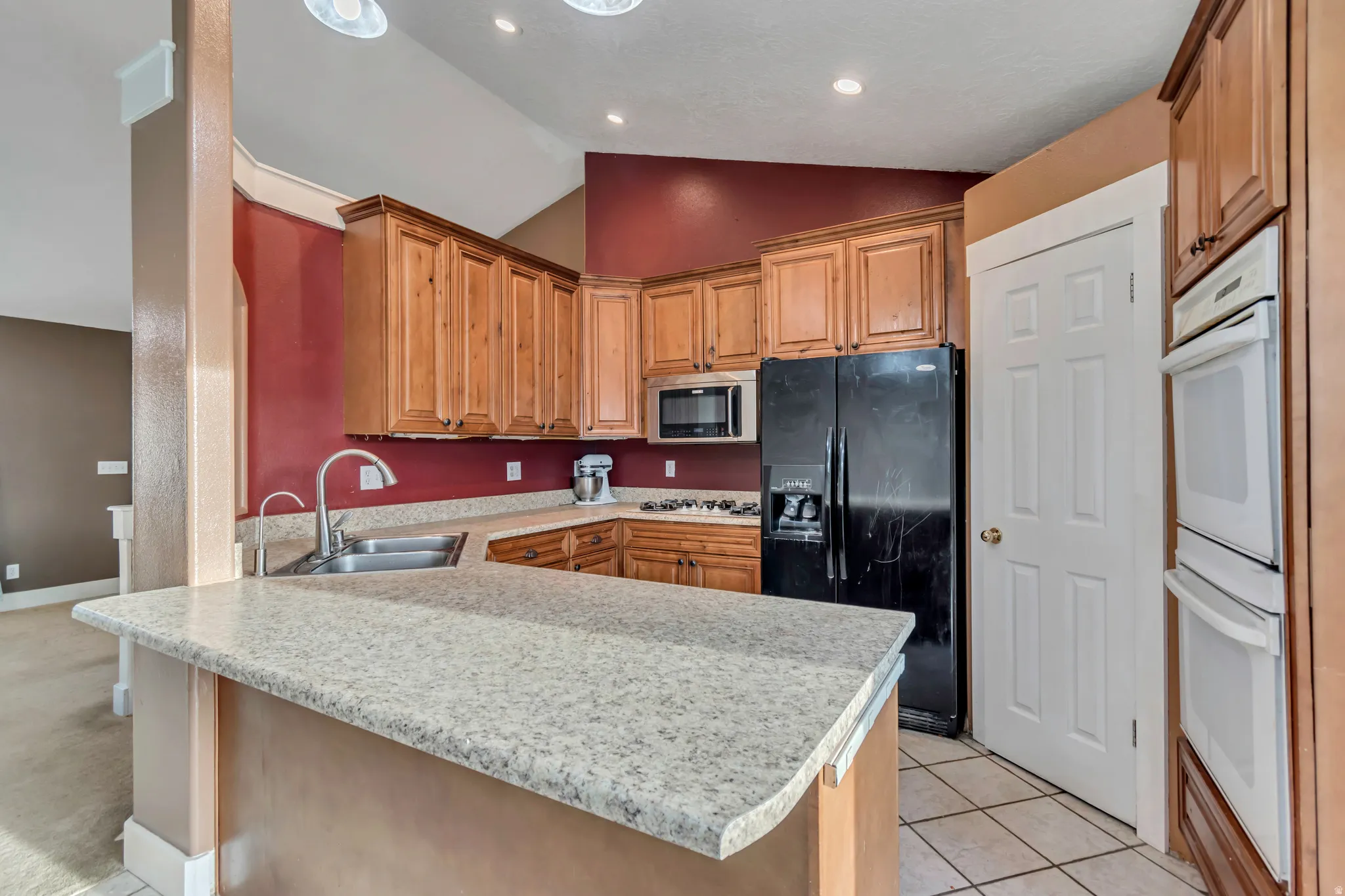 Kitchen with a peninsula, black refrigerator with ice dispenser, vaulted ceiling, double oven, and stainless steel microwave