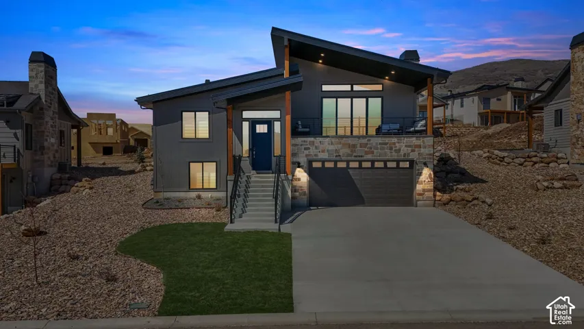 Modern architectural exterior featuring a dark gray facade, stone accents, a deep blue entry door, an upper-level balcony, and a two-car garage