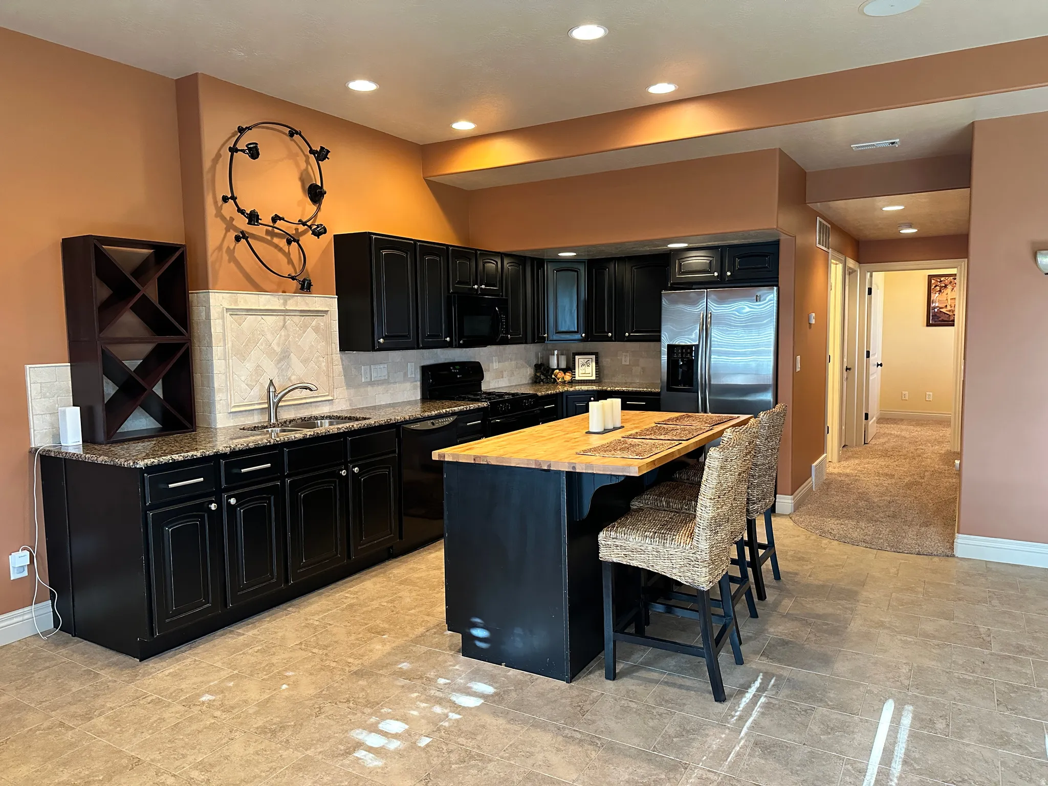 Kitchen with dark cabinetry, a kitchen bar, black appliances, granite countertops, and a kitchen island