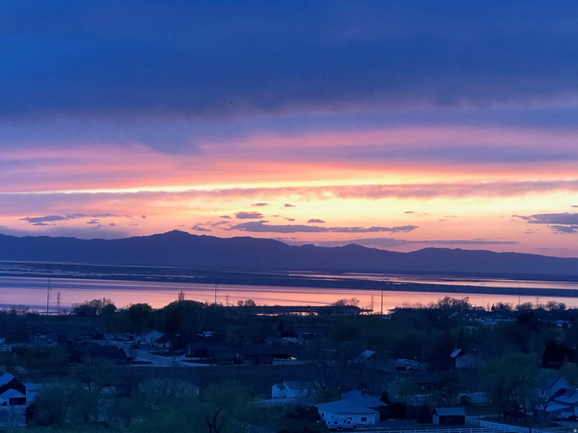 Expansive water body with distant mountain range under a vibrant, multi-hued sky