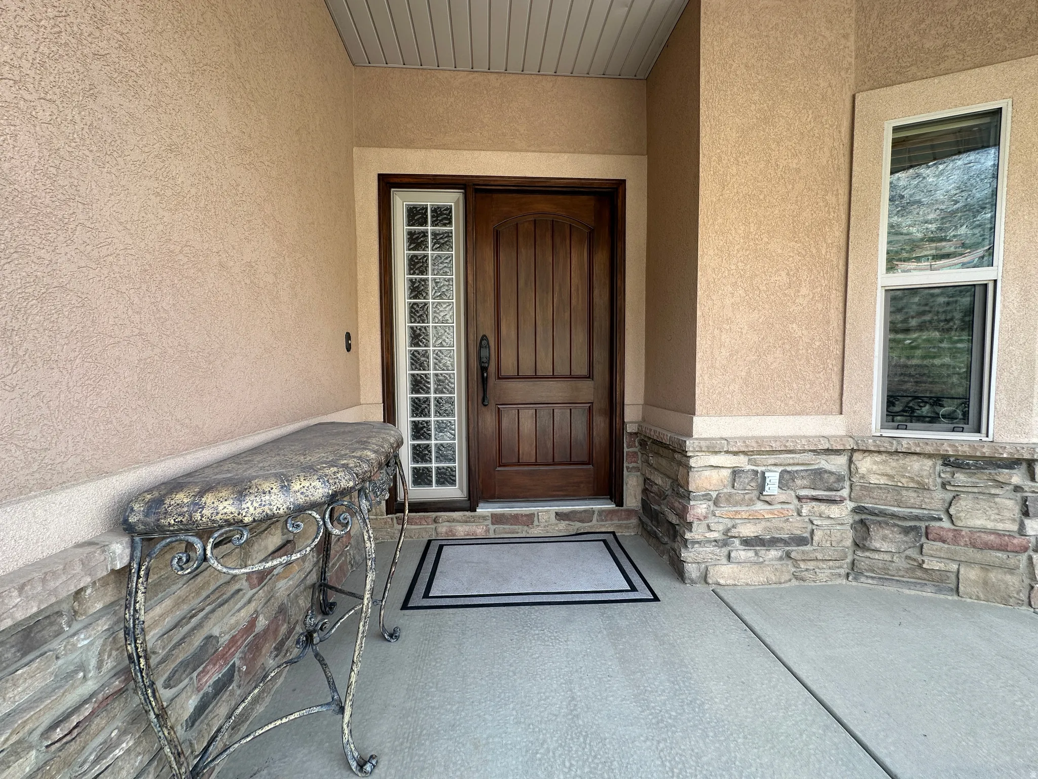 View of exterior entry featuring stucco siding, a porch, and stone siding