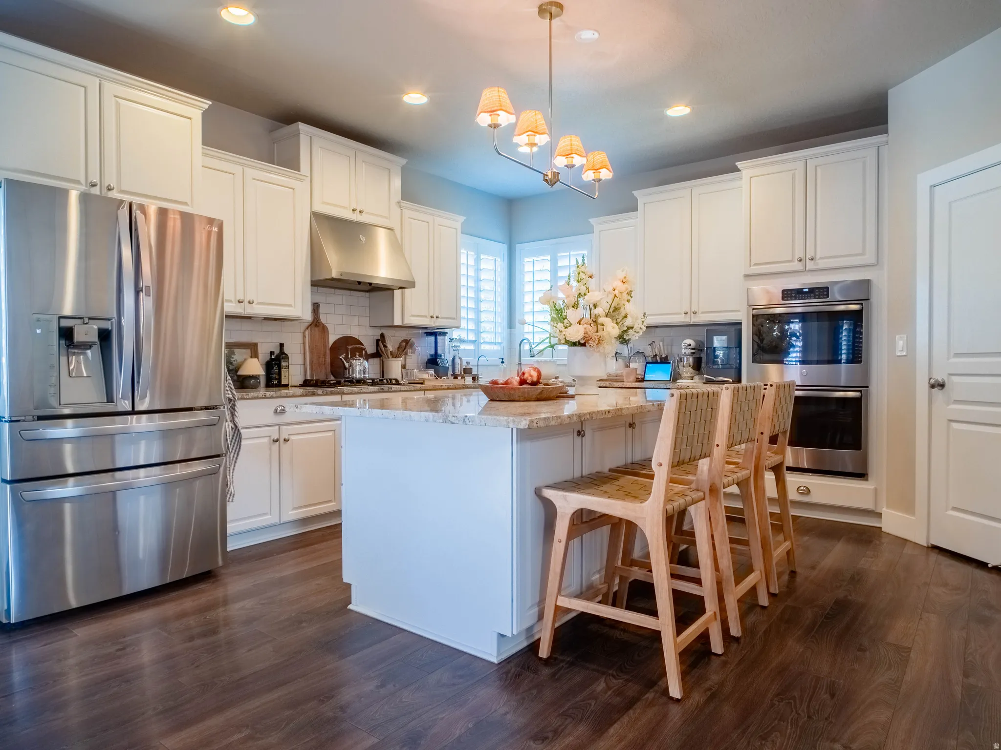 Kitchen with stainless steel appliances, a kitchen island, light stone counters, suspended lighting, and dark wood finished floors