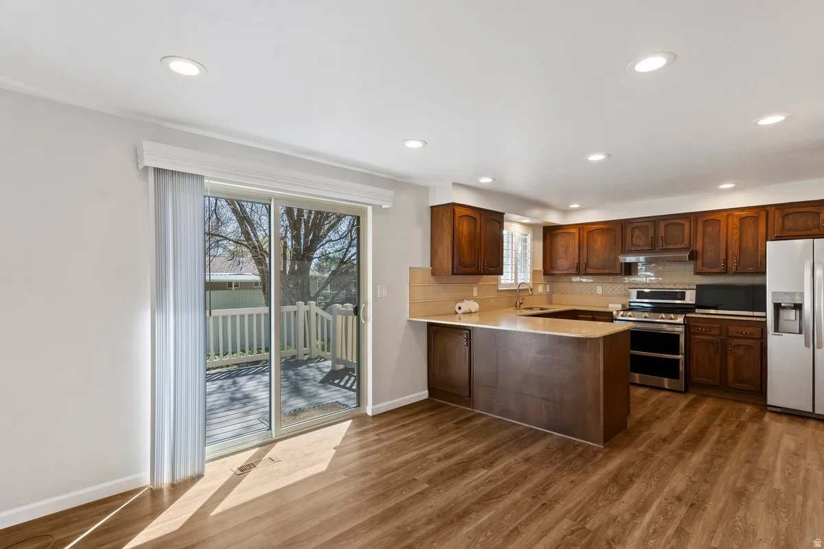 Kitchen featuring stainless steel appliances, a peninsula, recessed lighting, dark wood finished floors, and backsplash