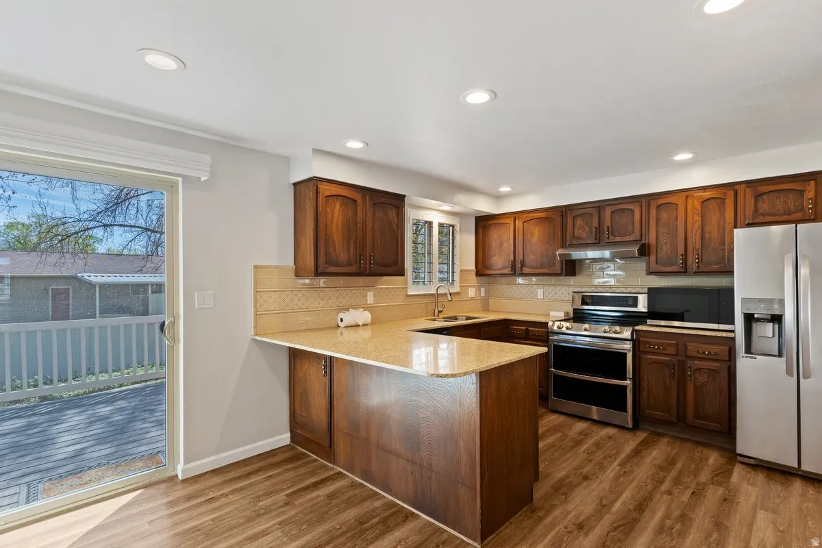 Kitchen featuring stainless steel appliances, a peninsula, backsplash, dark wood-style floors, and recessed lighting