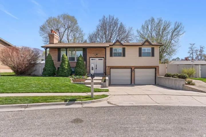 Bi-level home featuring brick siding, a garage, driveway, a chimney, and a gate
