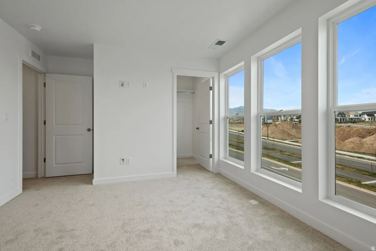 Unfurnished bedroom featuring a spacious closet, light colored carpet, and a mountain view