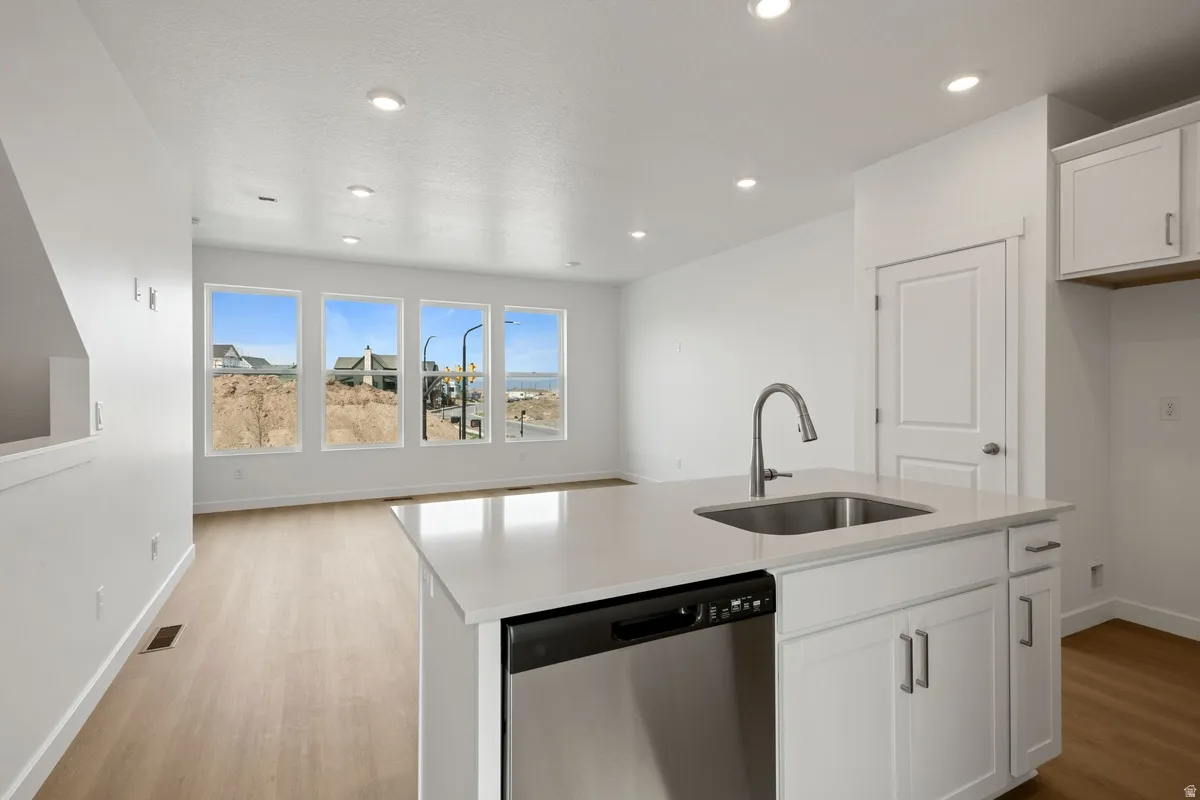 Kitchen with dishwasher, white cabinetry, a kitchen island with sink, light stone counters, and light wood-style flooring