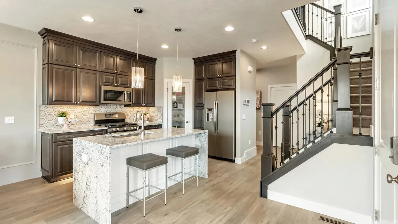 Kitchen featuring dark wood finish cabinetry, light stone countertops, stainless steel appliances, and an island with sink