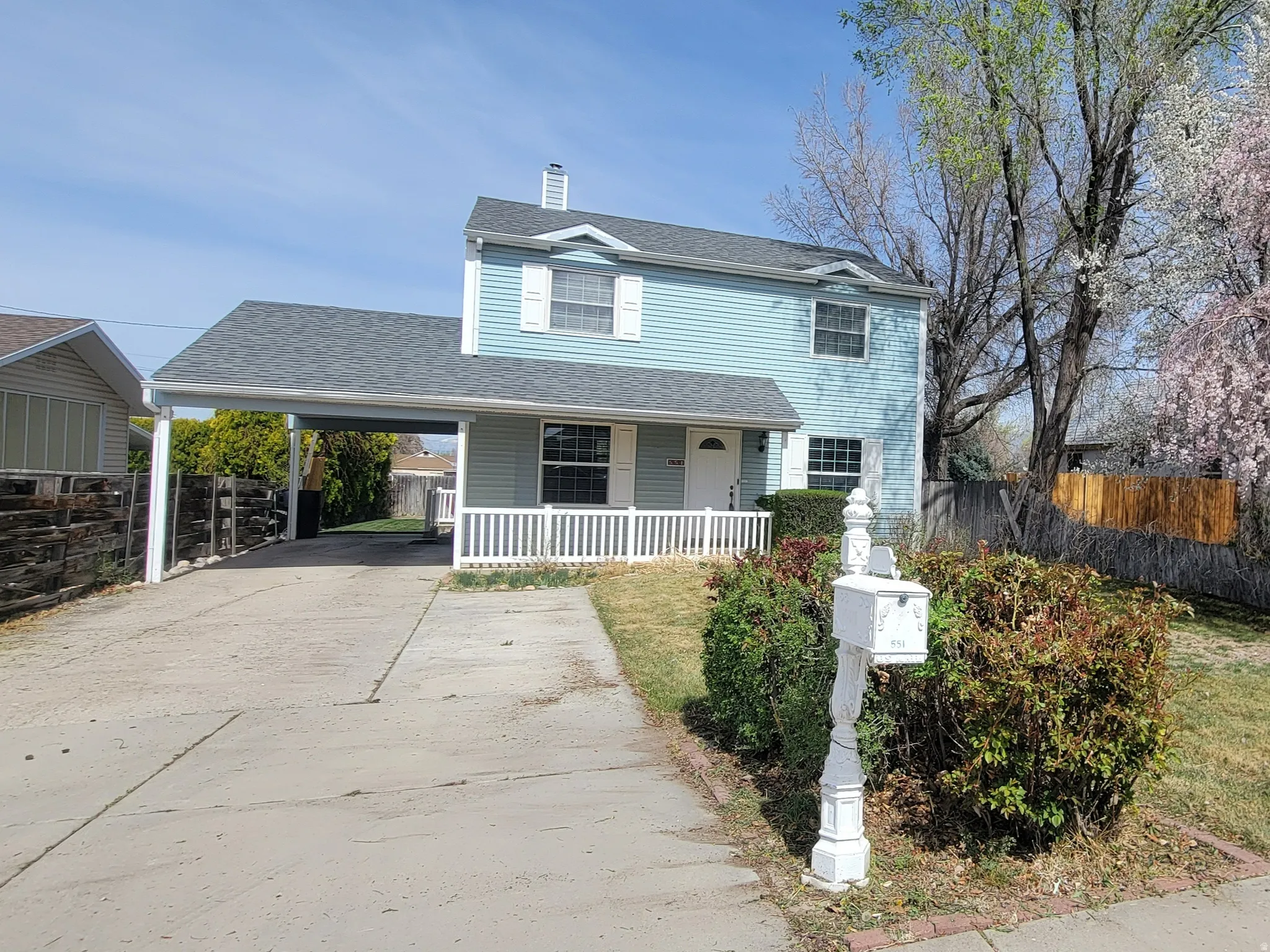 Traditional home featuring a carport, a porch, a chimney, driveway, and roof with shingles