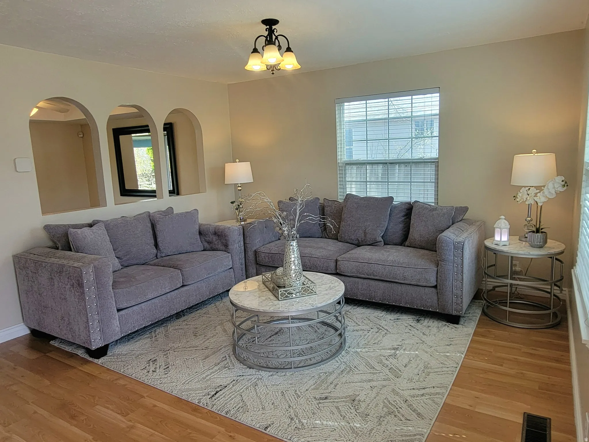 Living room featuring light wood-style flooring, arched walkways, and a chandelier