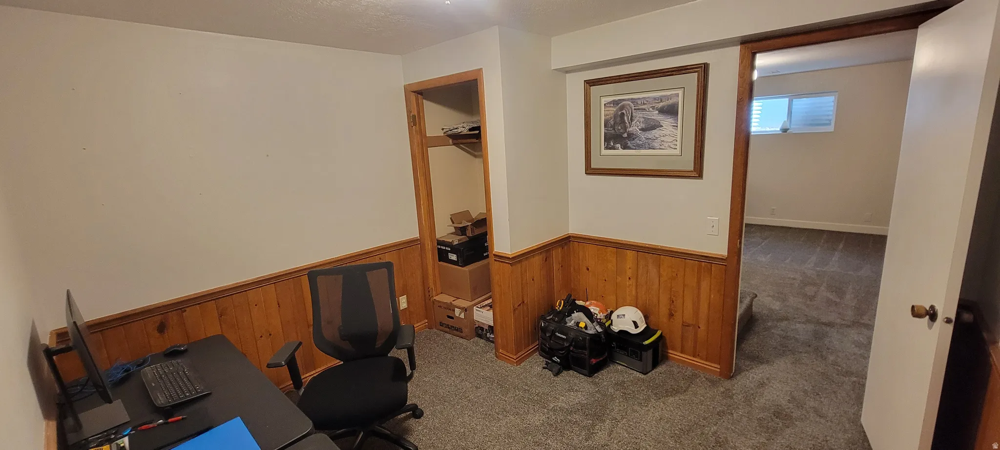 Home office featuring dark colored carpet, wooden walls, and wainscoting