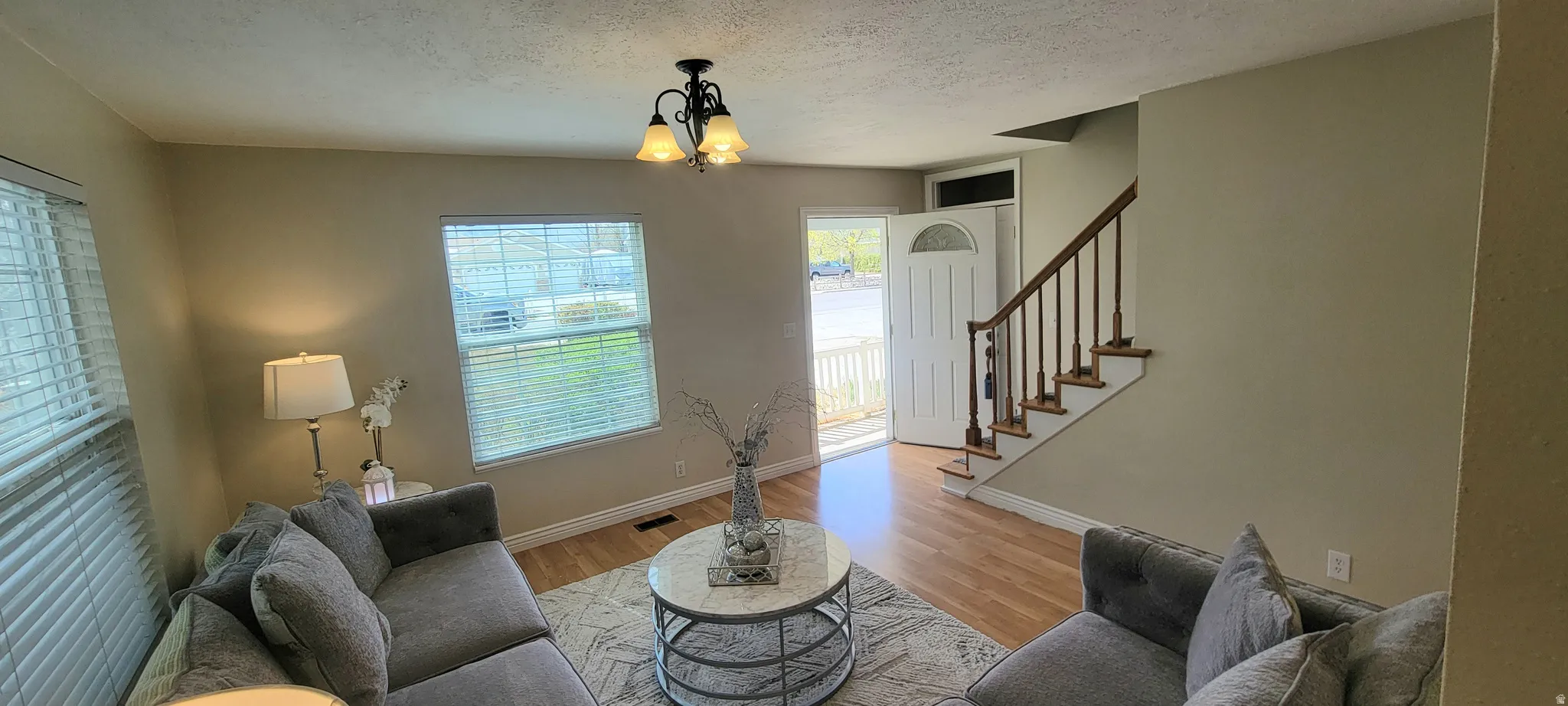 Living room with light wood-type flooring, a textured ceiling, and hanging lights