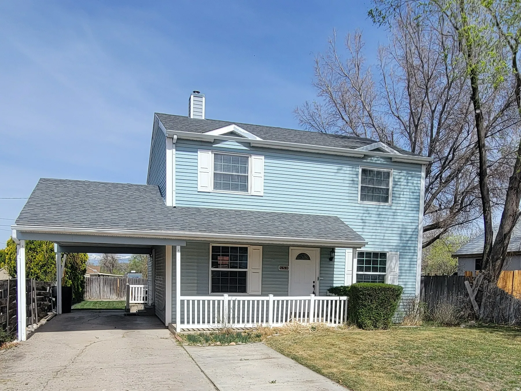 Traditional home featuring driveway, an attached carport, covered porch, a chimney, and roof with shingles