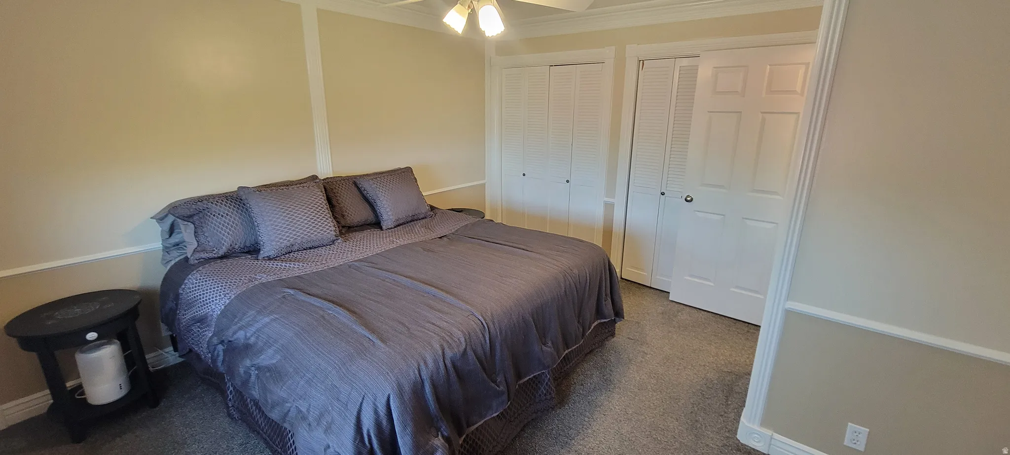 Bedroom featuring multiple closets, dark colored carpet, ceiling fan, and ornamental molding