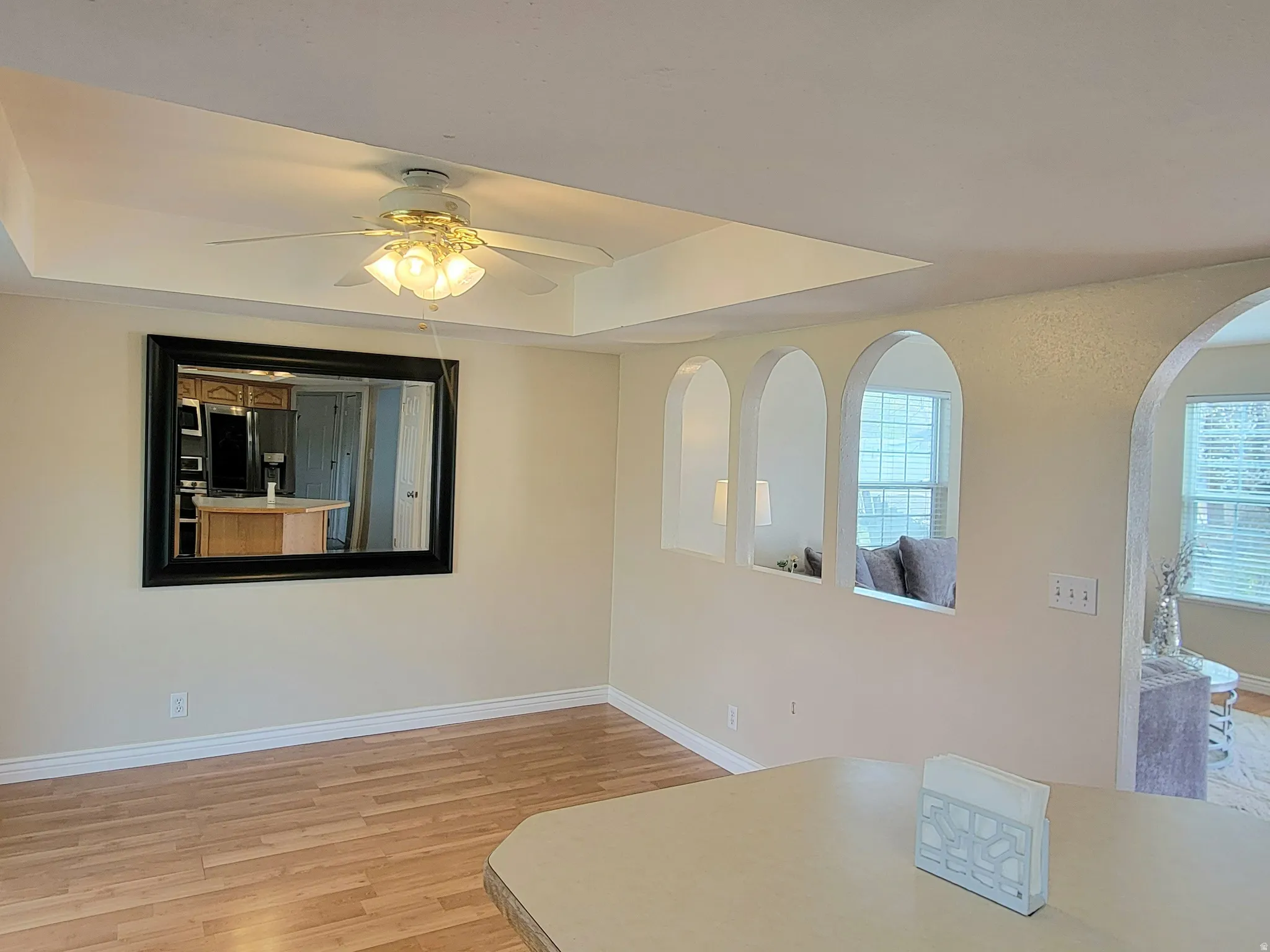 Unfurnished dining area featuring light wood-type flooring, ceiling fan, and a raised ceiling