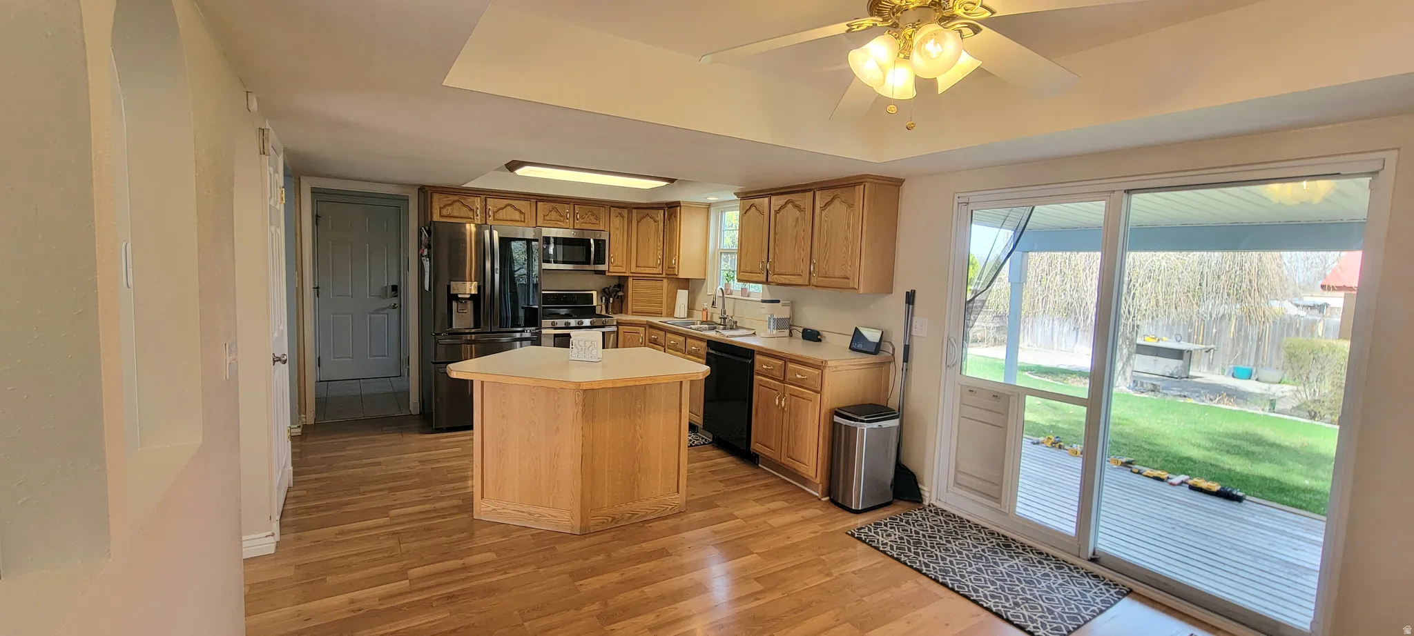 Kitchen with light countertops, a kitchen island, black appliances, a ceiling fan, and light wood-type flooring