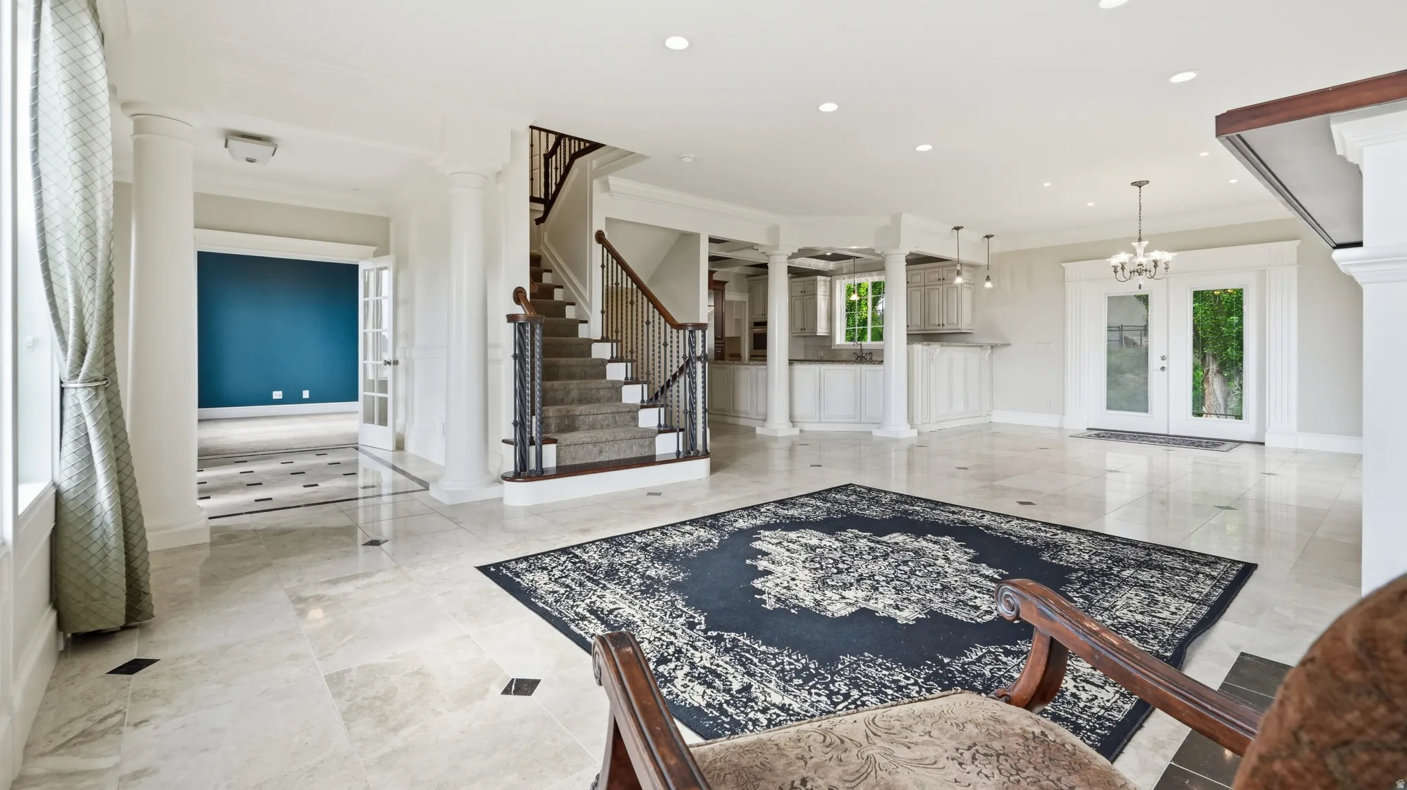 Expansive interior with polished tile flooring, grand staircase with dark wood handrail, white interior columns, recessed lighting, and French doors