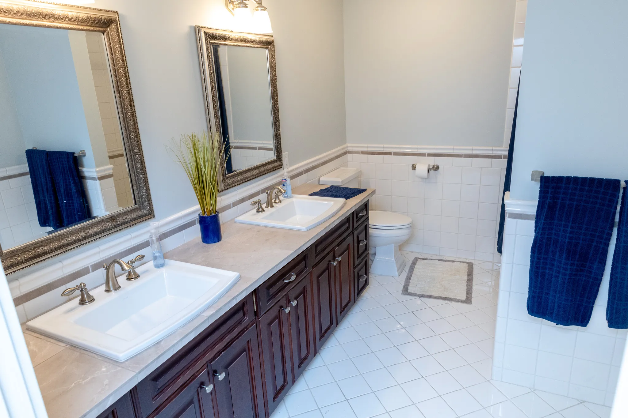 Bathroom with double vanity, wainscoting, tile walls, and light tile patterned floors