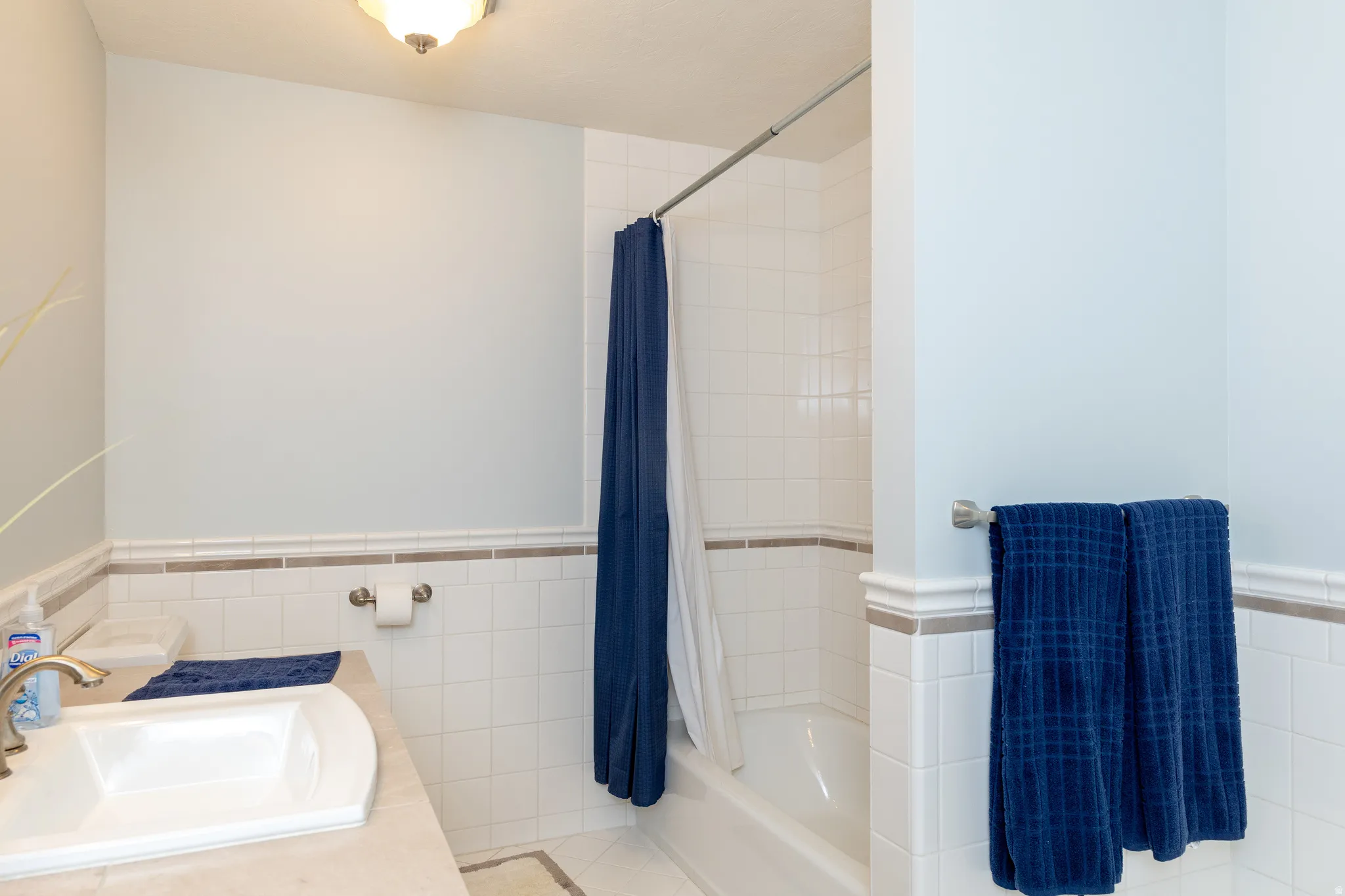 Bathroom featuring tile walls, a wainscoted wall, vanity, shower / tub combo, and tile patterned flooring