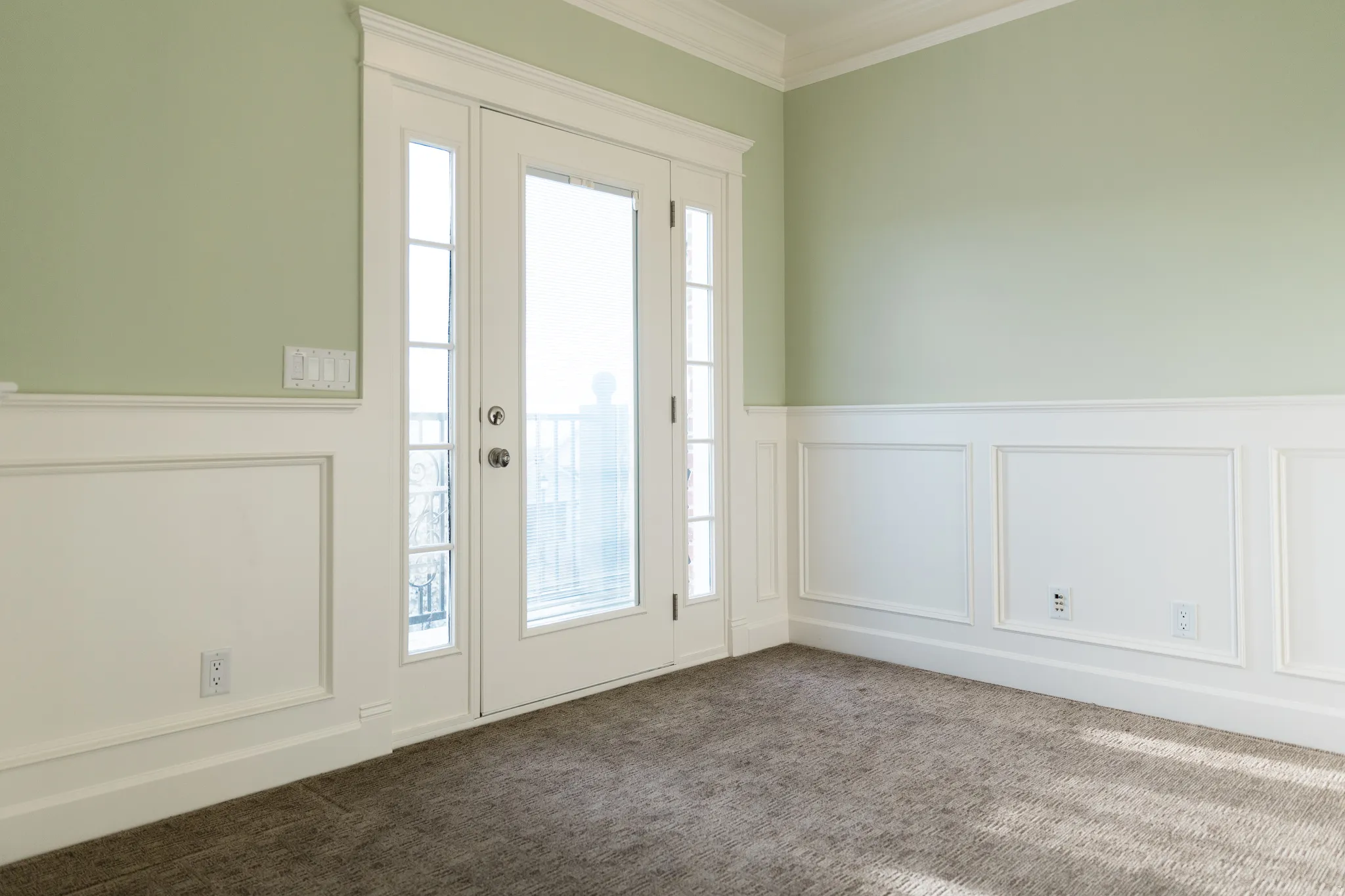 Doorway to outside with a decorative wall, ornamental molding, wainscoting, and carpet flooring