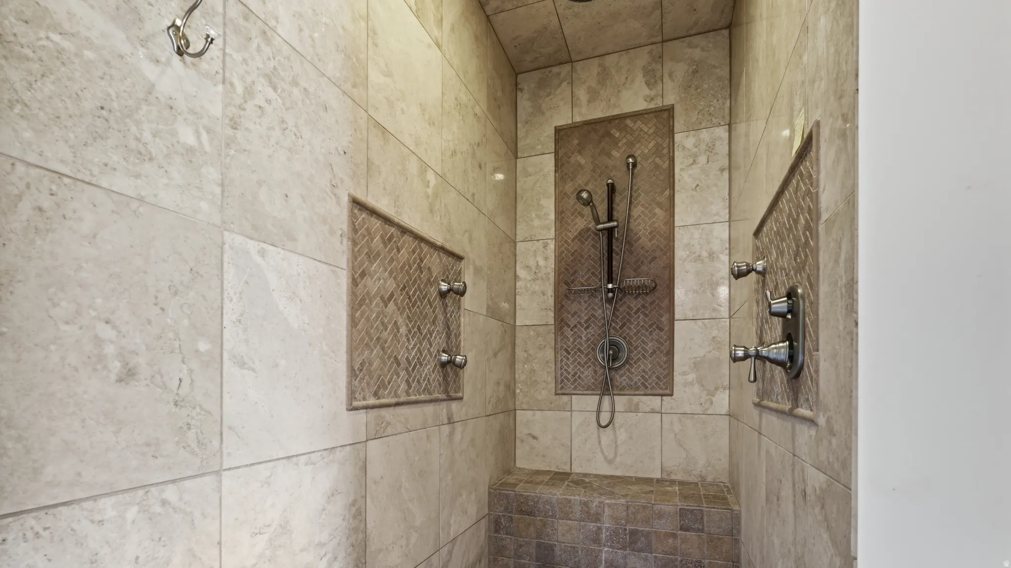 Spa-inspired walk-in shower featuring multiple showerheads with individual controls, stone tile surround in neutral tones, and a built-in bench niche