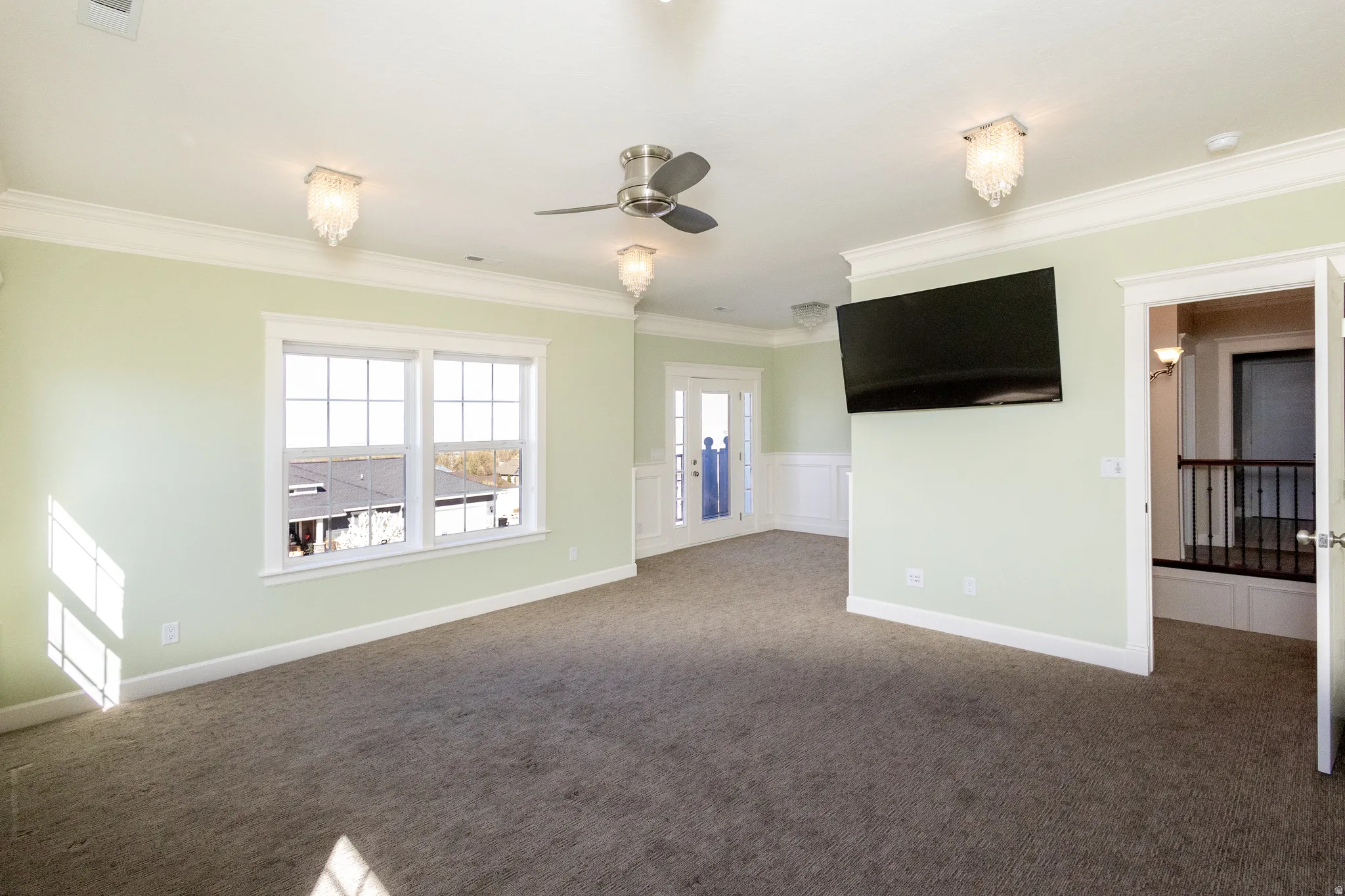 Carpeted empty room featuring wainscoting, ornamental molding, a decorative wall, and a ceiling fan