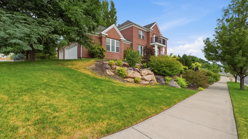 Brick Colonial situated on a sloped lot with mature landscaping and established trees