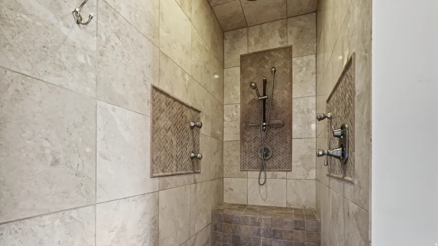Spa-inspired walk-in shower featuring multiple showerheads with individual controls, stone tile surround in neutral tones, and a built-in bench niche