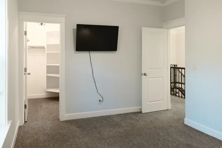 Unfurnished bedroom featuring a walk in closet, dark carpet, and ornamental molding
