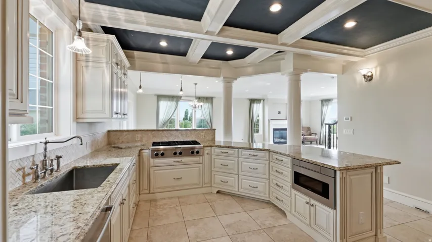 Gourmet kitchen with coffered ceiling, stainless steel appliances, granite countertops, and tile flooring