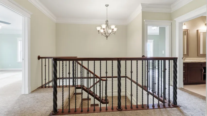 Elegant upper-level landing featuring a wrought-iron stair railing with turned balusters, neutral wall finishes, recessed ceiling lighting, and a coordinating chandelier