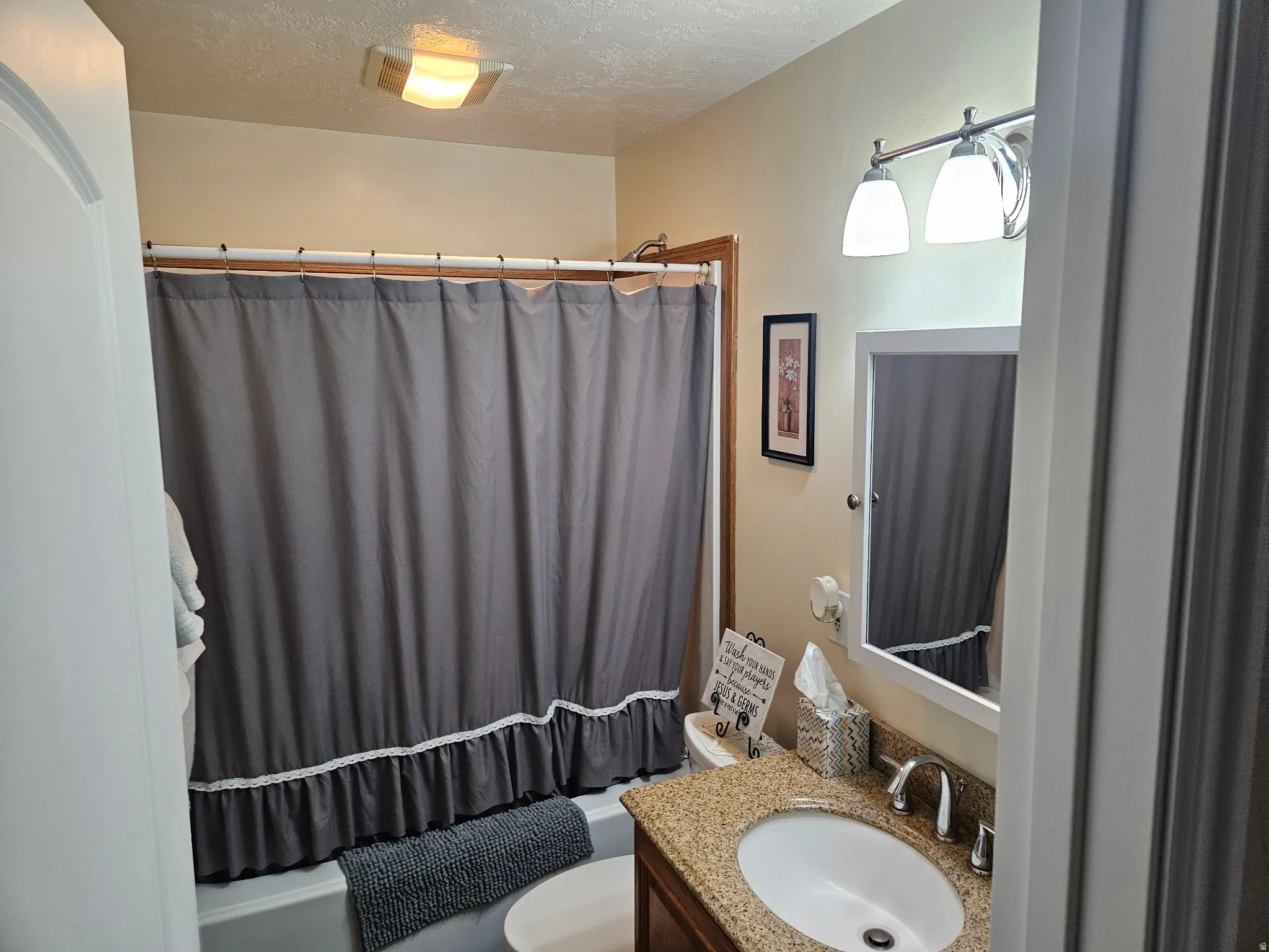 Bathroom with vanity, a textured ceiling, and shower / tub combo