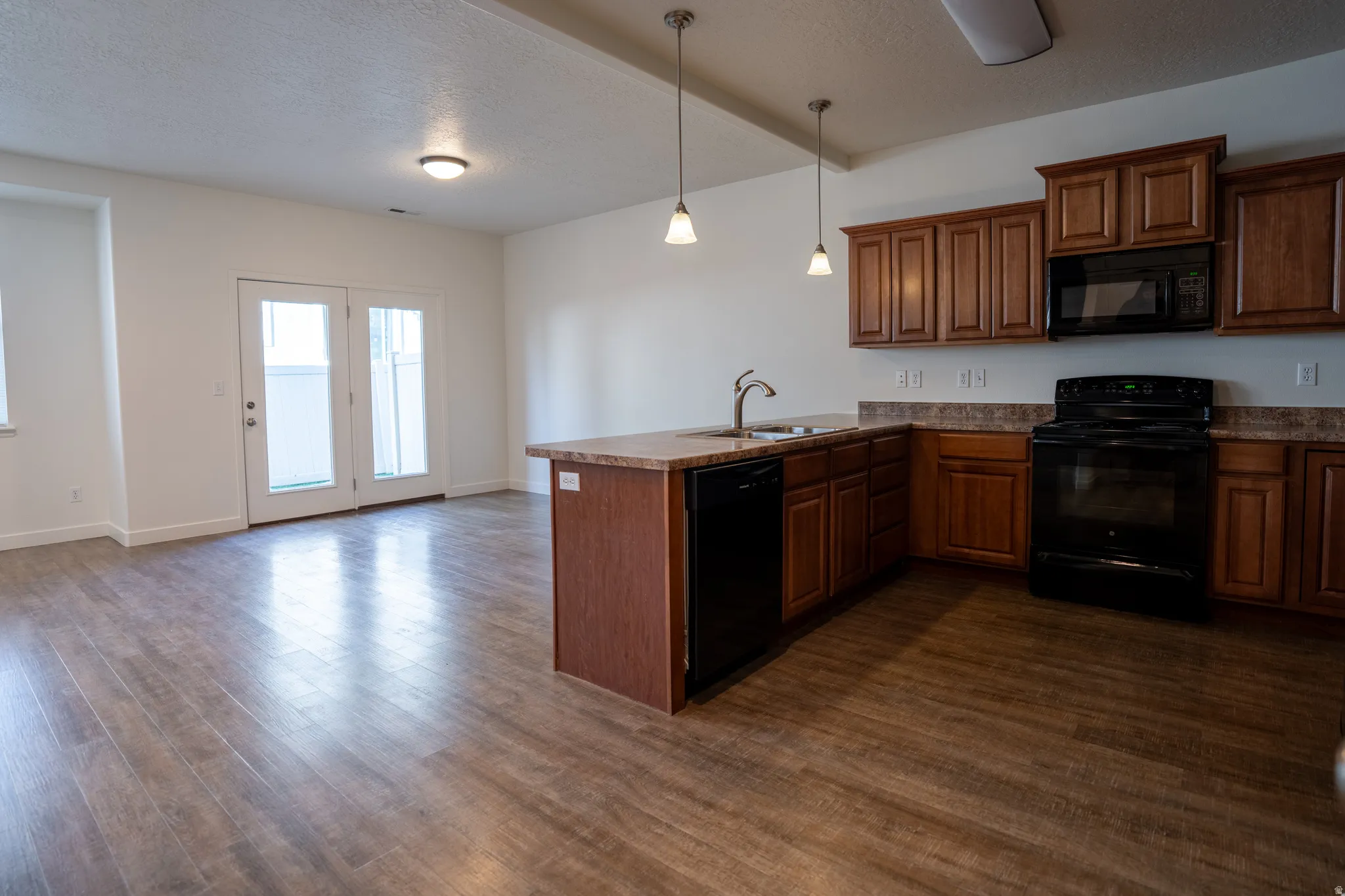 Kitchen with a peninsula, black appliances, a textured ceiling, hanging light fixtures, and dark wood-type flooring