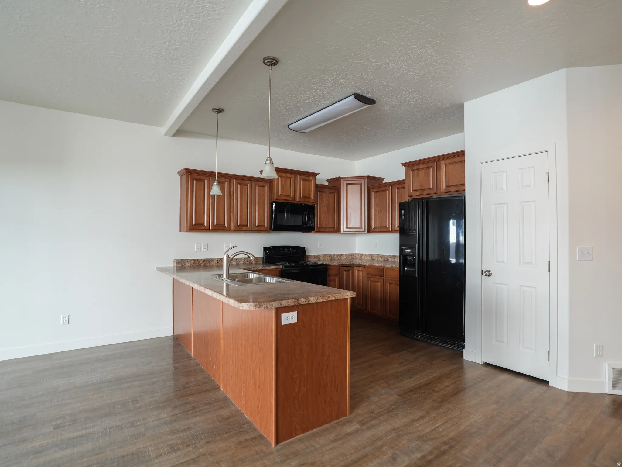Kitchen with wood finish cabinets, a peninsula, black appliances, hanging light fixtures, and dark wood finished floors