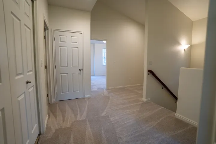 Hall with an upstairs landing, light colored carpet, and vaulted ceiling