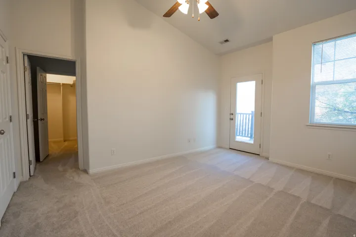 Empty room featuring light carpet, ceiling fan, and vaulted ceiling