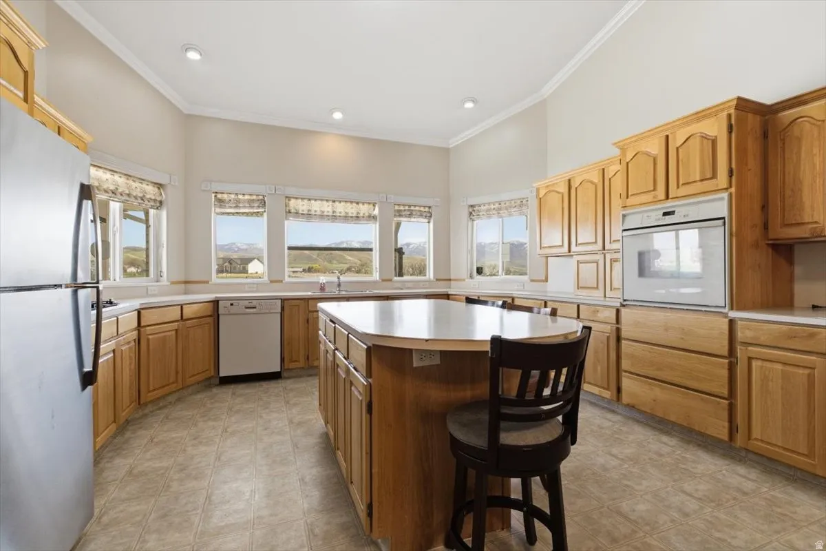 Kitchen featuring light countertops, white appliances, a breakfast bar, a kitchen island, and ornamental molding
