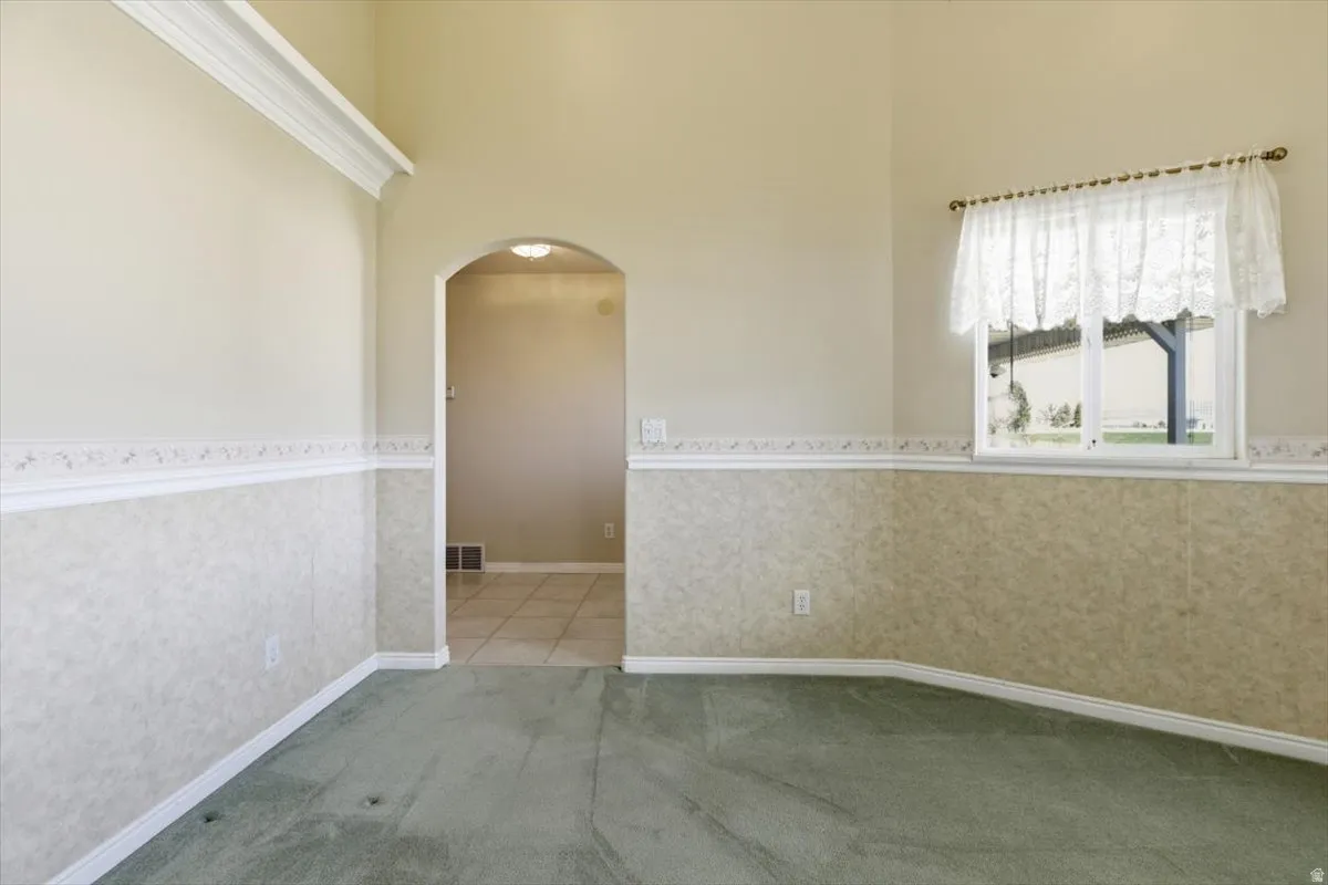 Unfurnished room with arched walkways, wallpapered walls, light carpet, wainscoting, and a high ceiling