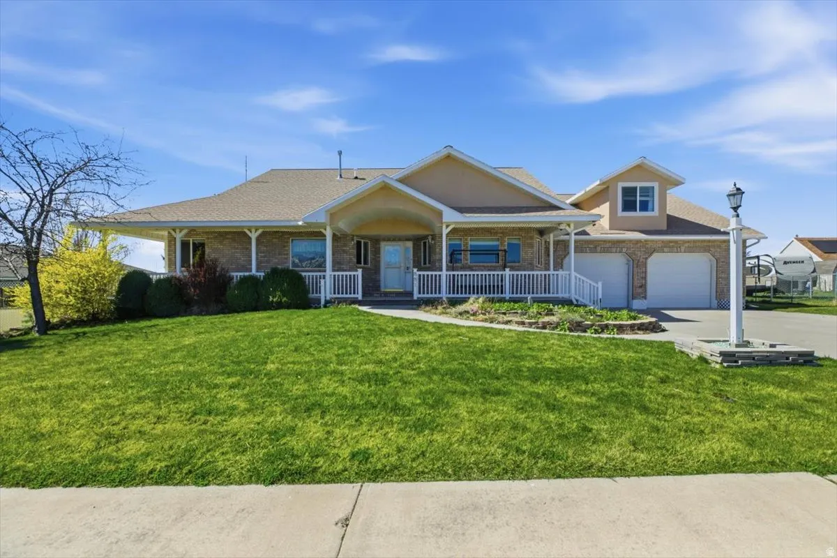 View of front of house with a porch, a front yard, a garage, driveway, and brick siding