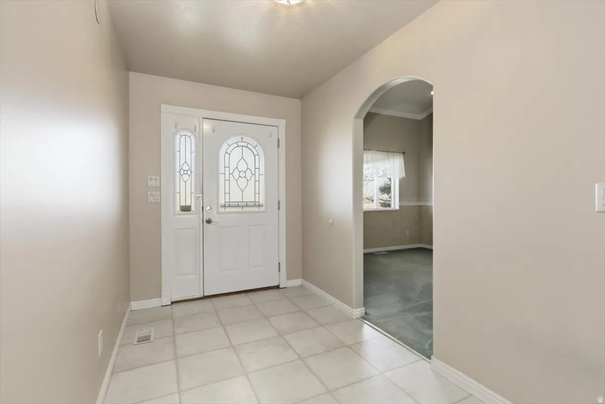 Foyer featuring arched walkways, light tile patterned flooring, and light colored carpet