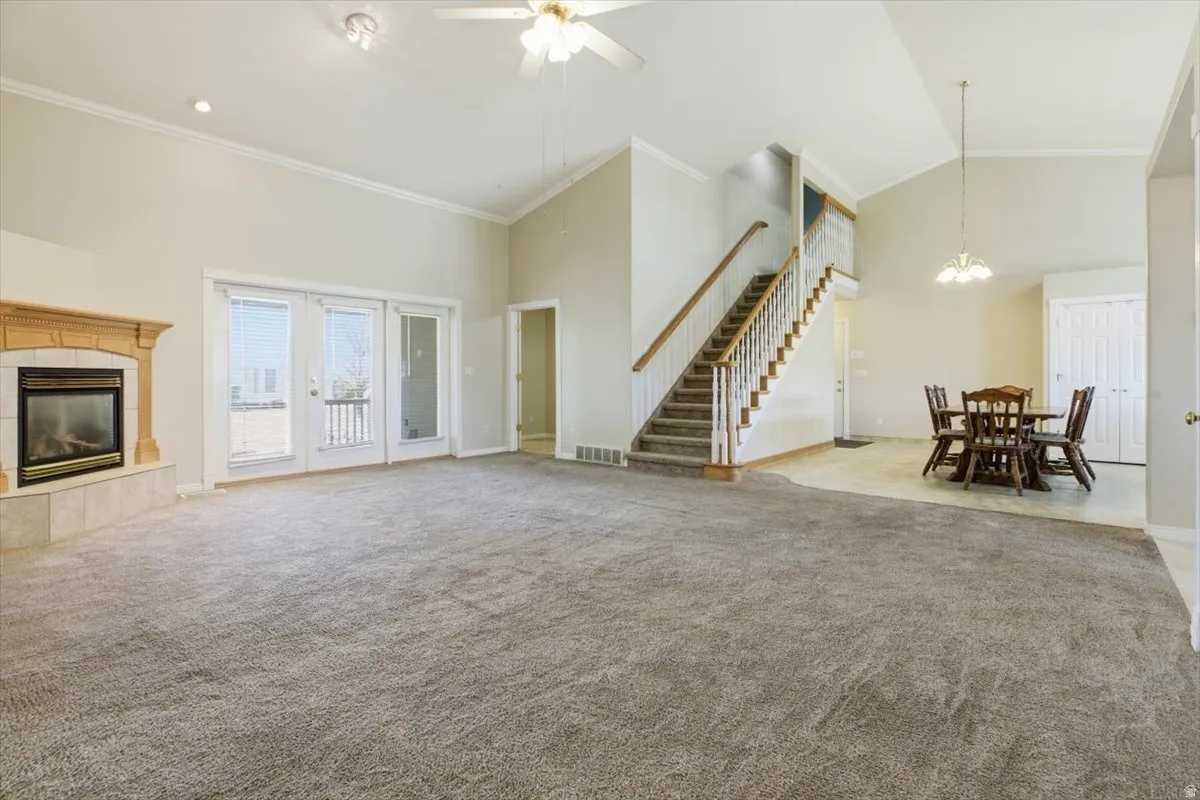 Unfurnished living room with ornamental molding, light carpet, a ceiling fan, a tiled fireplace, and suspended lighting